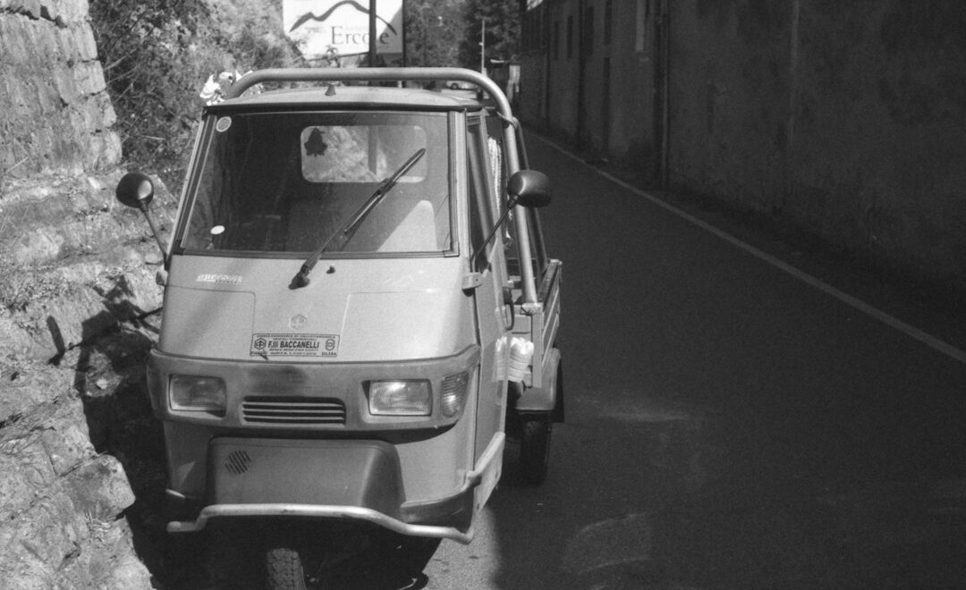 Piaggio Ape -kolmipyörä pysäköitynä kapealla kadulla kivimuurin vieressä